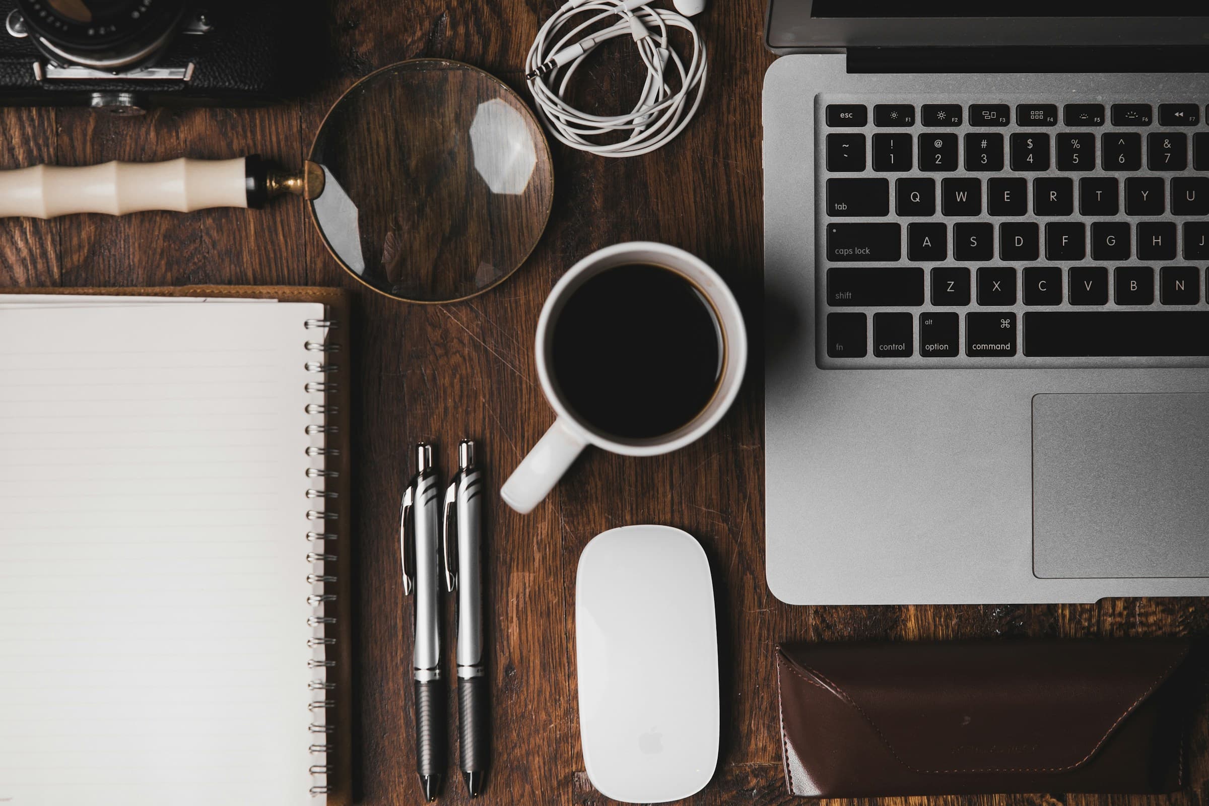 A tidy desk with a laptop, notebook and coffee.